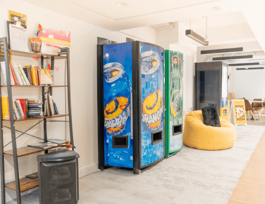 Espace détente avec distributeurs de boissons, bibliothèque et pouf jaune chez Hiptown Place de la Bourse à Paris