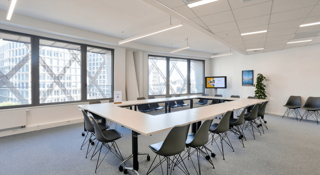 Salle de réunion moderne à Rennes EuroRennes avec une table en U, chaises ergonomiques et grandes fenêtres offrant une vue sur l’architecture extérieure unique