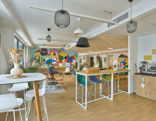 Espace de coworking à Rennes EuroRennes avec tables hautes, chaises colorées, luminaires modernes et une fresque murale artistique pour une ambiance créative