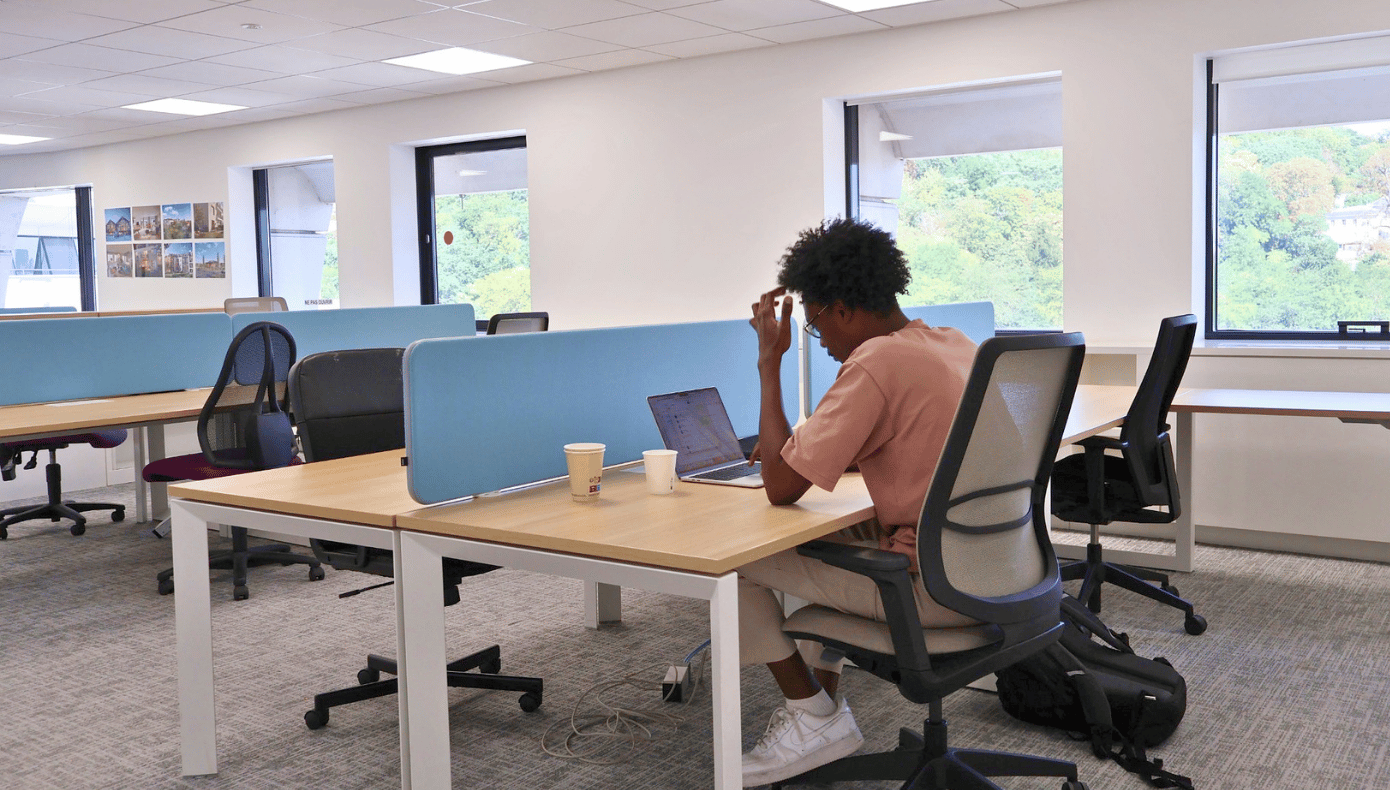 Personne travaillant sur ordinateur portable dans l’open space Hiptown à Sèvres, avec bureaux partagés et grandes fenêtres.