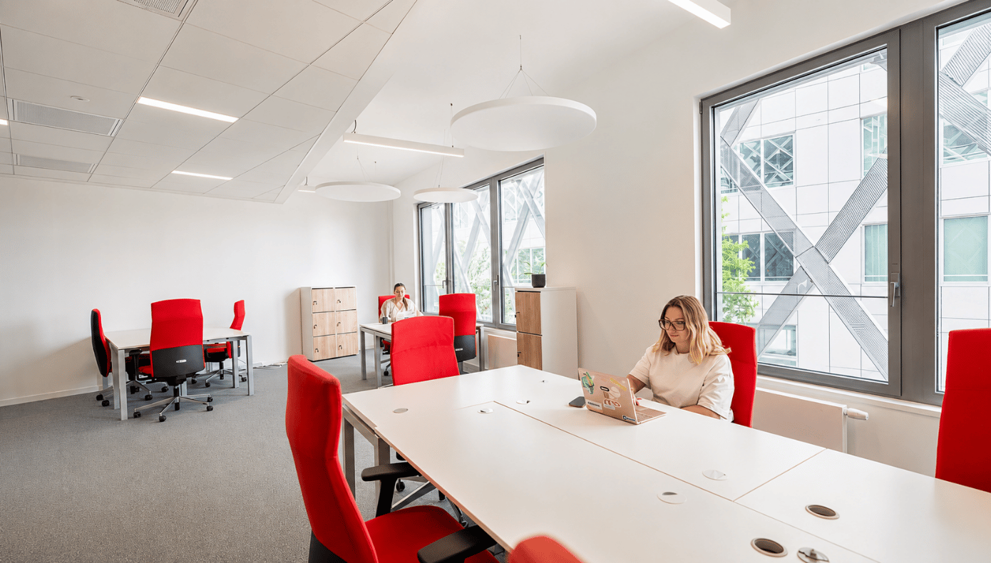 Bureau privatif lumineux à Hiptown EuroRennes avec postes de travail, fauteuils rouges et grandes fenêtres.