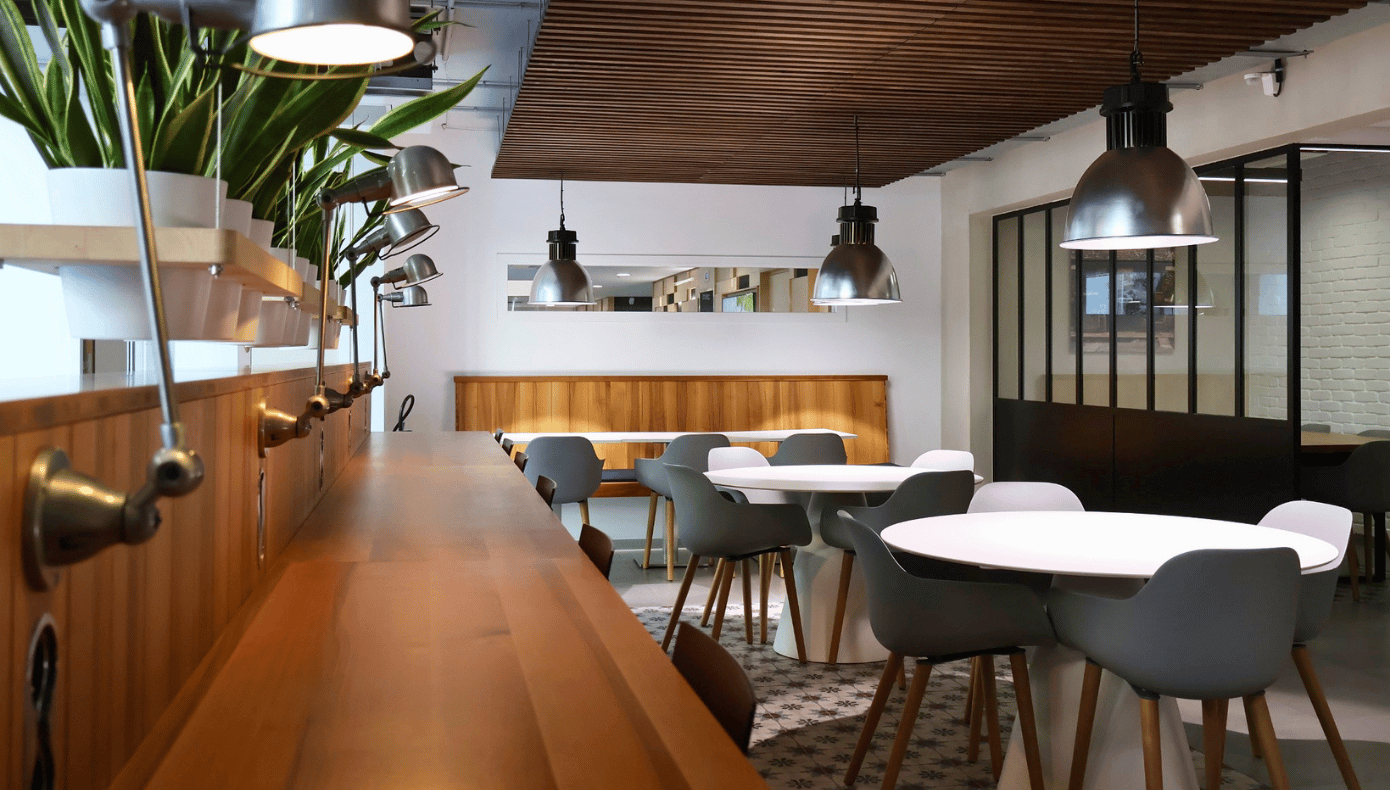 Cafétéria Hiptown à Sèvres avec tables, assises, comptoir en bois et luminaires suspendus.