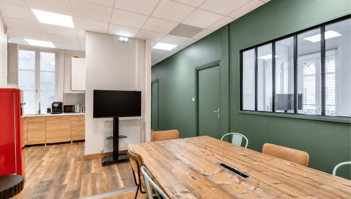 Espace cuisine Hiptown à Lyon avec grande table en bois, chaises, kitchenette équipée et écran sur pied