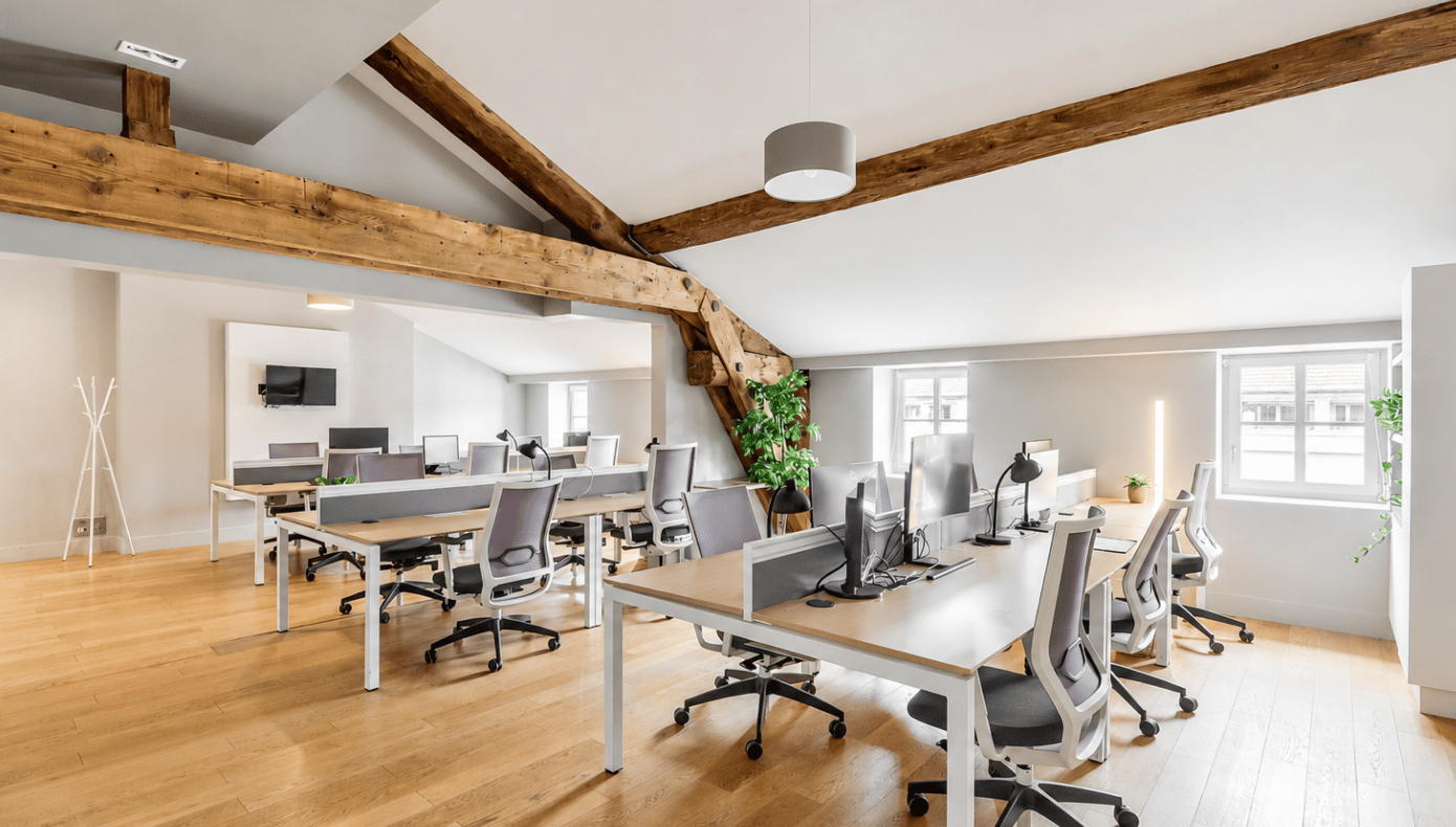 Bureau privatif avec plusieurs postes de travail, écrans, chaises de bureau et poutres en bois apparentes.