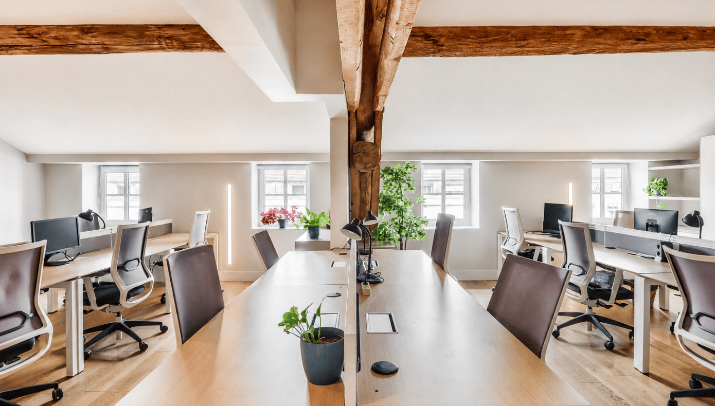 Bureau privatif à Presqu’île Opéra avec postes de travail, table centrale, plantes et poutres en bois.
