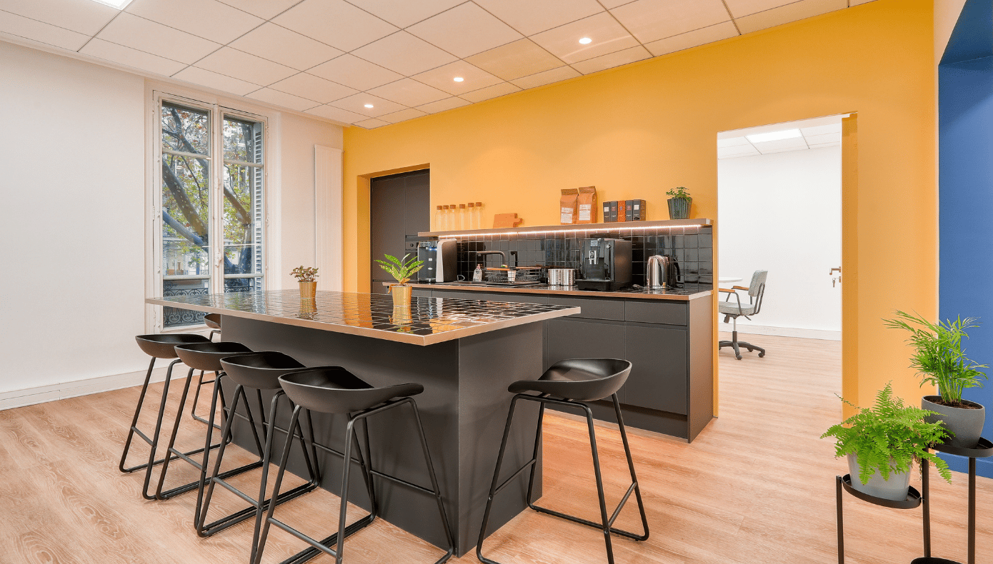 Cuisine équipée de l’espace Haussmann Cuisine partagée avec îlot central, tabourets et espace café dans les bureaux Hiptown Haussmann à Paris.