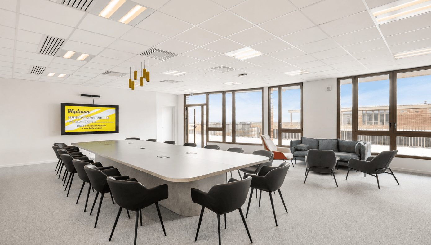 Salle de réunion Hiptown Cyberplace à Rennes avec grande table, écran mural, nombreux sièges et espace lounge.