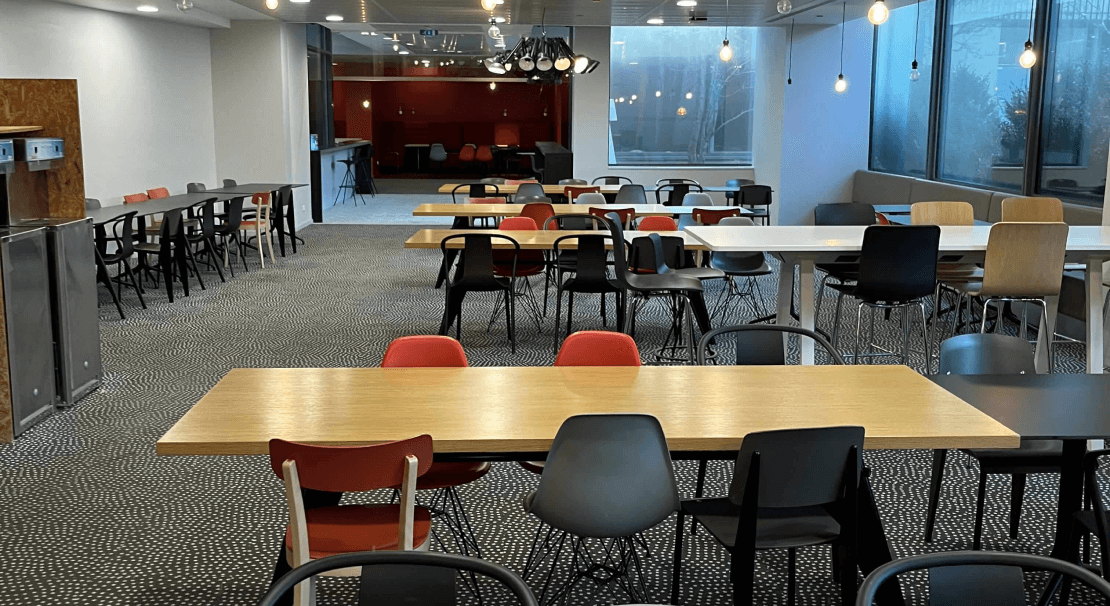 Cafetaria Hiptown : espace moderne avec table en bois, chaises confortables et grande baie vitrée lumineuse