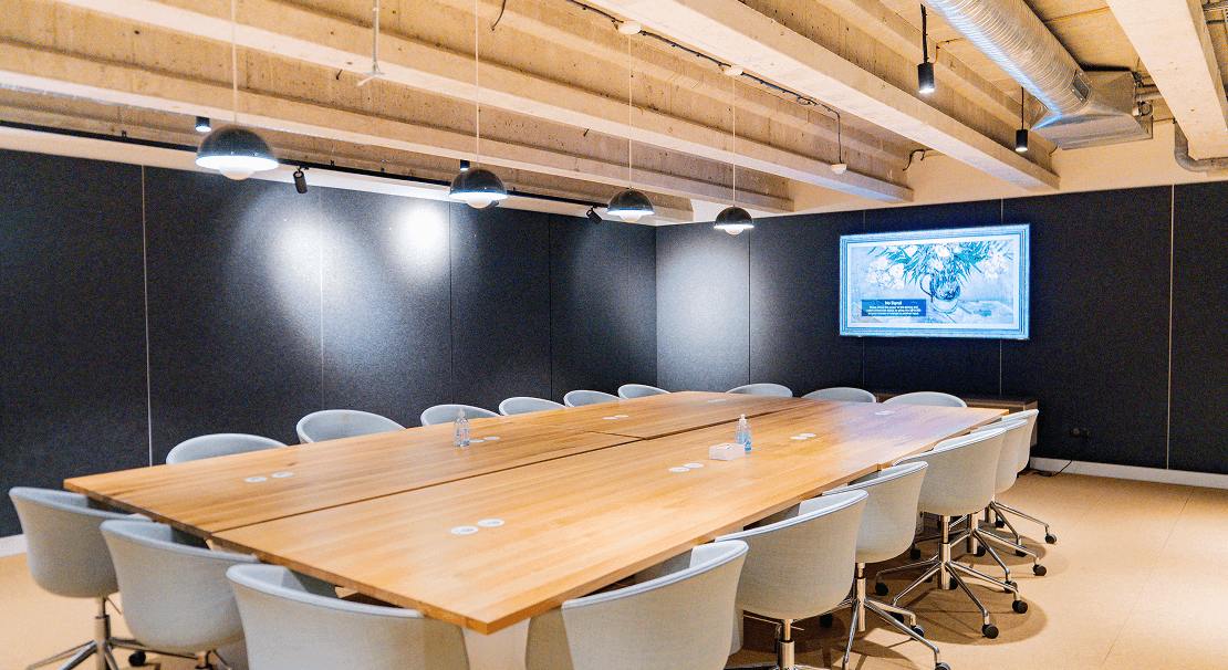 Grande salle de réunion moderne avec une table en bois, des chaises ergonomiques et un écran mural affichant une présentation