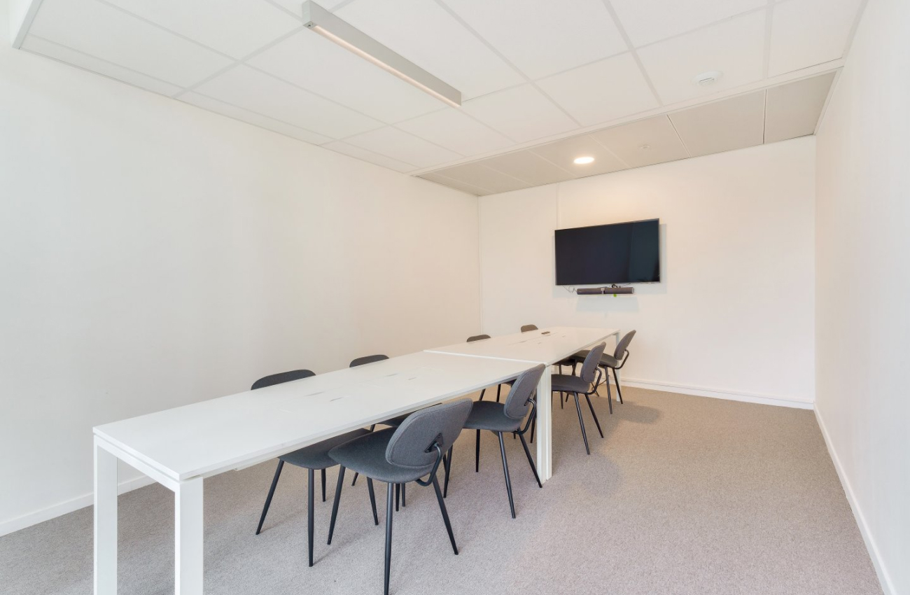 Salle de réunion moderne avec une grande table blanche, des chaises grises et un écran mural au Quai de Paludate à Bordeaux