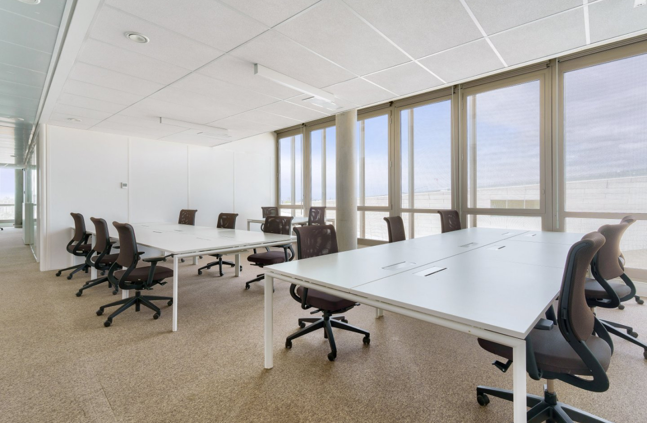 Salle de bureau moderne et lumineuse avec des grandes tables blanches, des chaises ergonomiques et des fenêtres du sol au plafond au Quai de Paludate à Bordeaux.