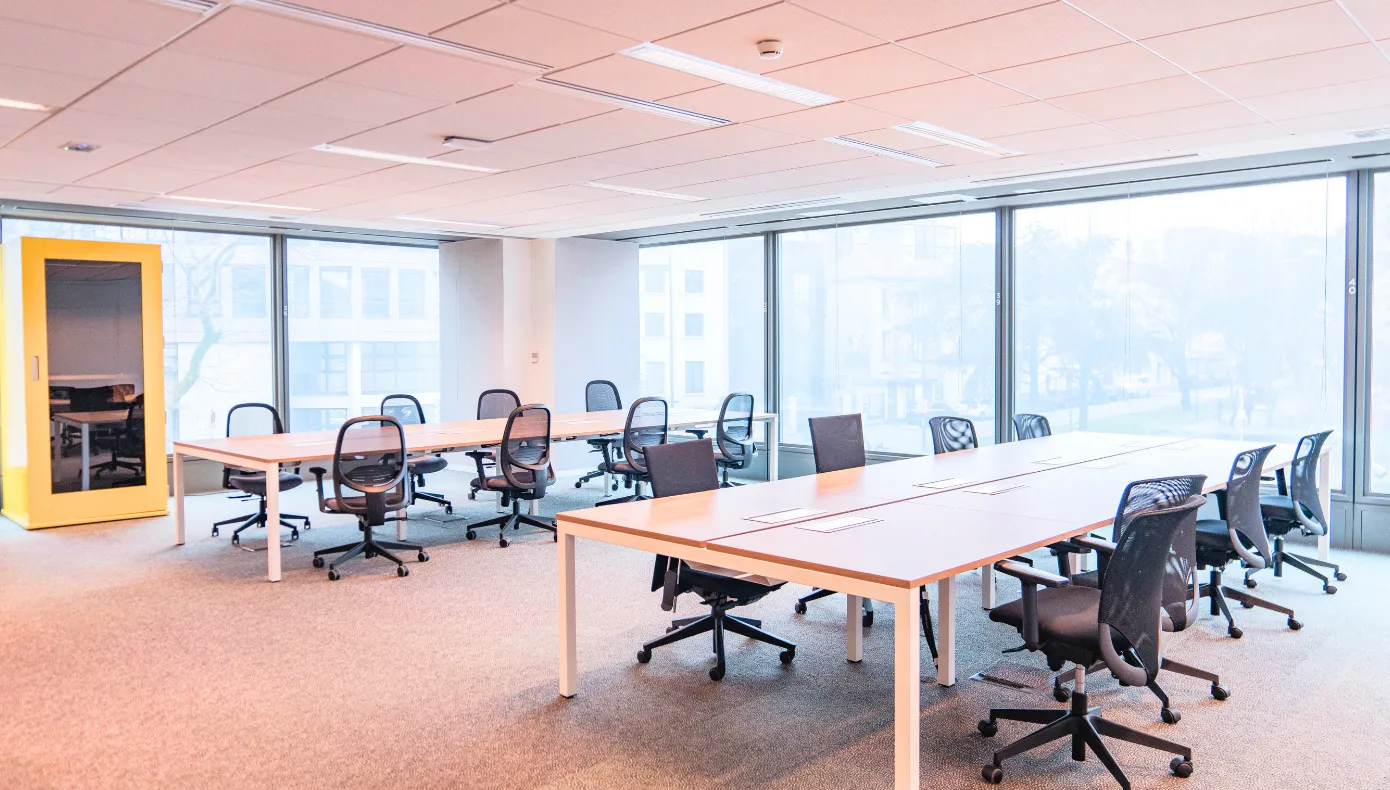 Espace de travail partagé à Montreuil avec longues tables, fauteuils de bureau et cabine individuelle.