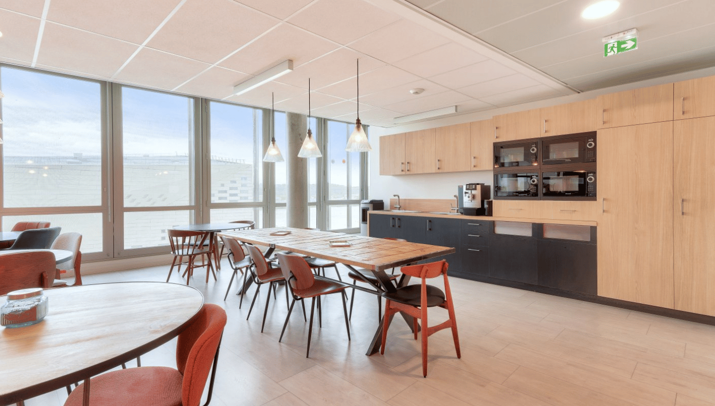Espace repas Hiptown à Bordeaux avec grande table, chaises, cuisine équipée et baies vitrées.