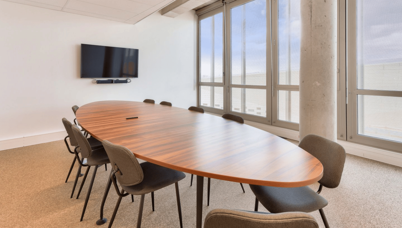Salle de réunion avec grande table ovale, chaises, écran mural et baies vitrées chez Hiptown à Bordeaux.