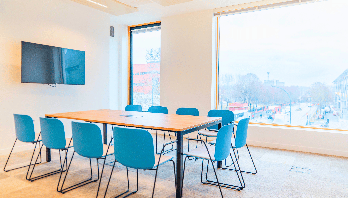 Salle de réunion lumineuse à Pantin avec grande table, chaises bleues, écran mural et baies vitrées donnant sur la ville.