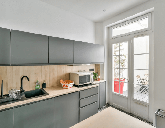 Cuisine moderne à Hiptown Lyon Brotteaux avec placards gris, plan de travail en bois, évier noir et accès à une terrasse extérieure