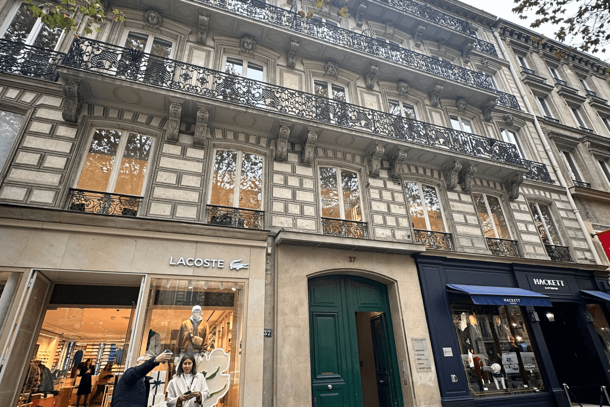 Façade d'un immeuble haussmannien à Paris Madeleine, avec une boutique Lacoste et Hackett au rez-de-chaussée, symbole d'un établissement prestigieux