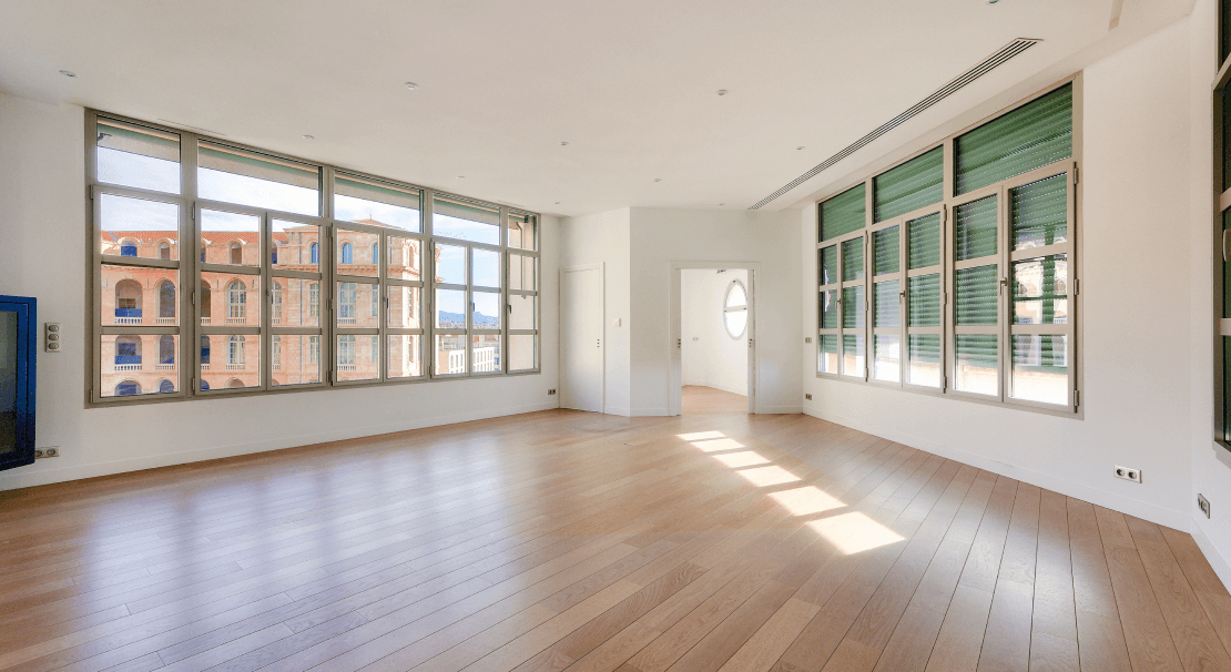 Grand espace de bureaux lumineux avec parquet, larges fenêtres offrant une vue dégagée sur des bâtiments historiques à Marseille