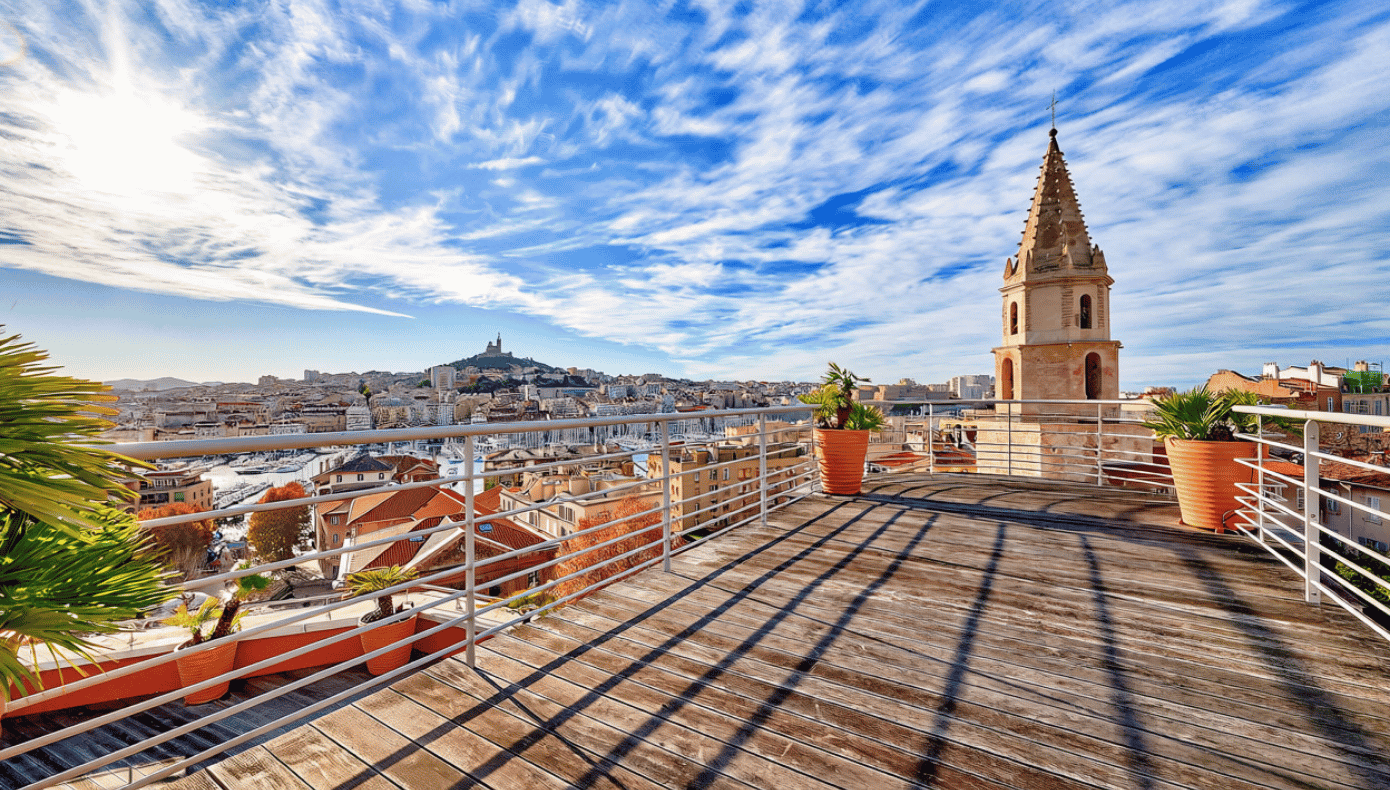 Vue sur Marseille depuis le rooftop Hiptown Panier Terrasse rooftop de Hiptown Panier avec vue panoramique sur les toits de Marseille et Notre-Dame de la Garde