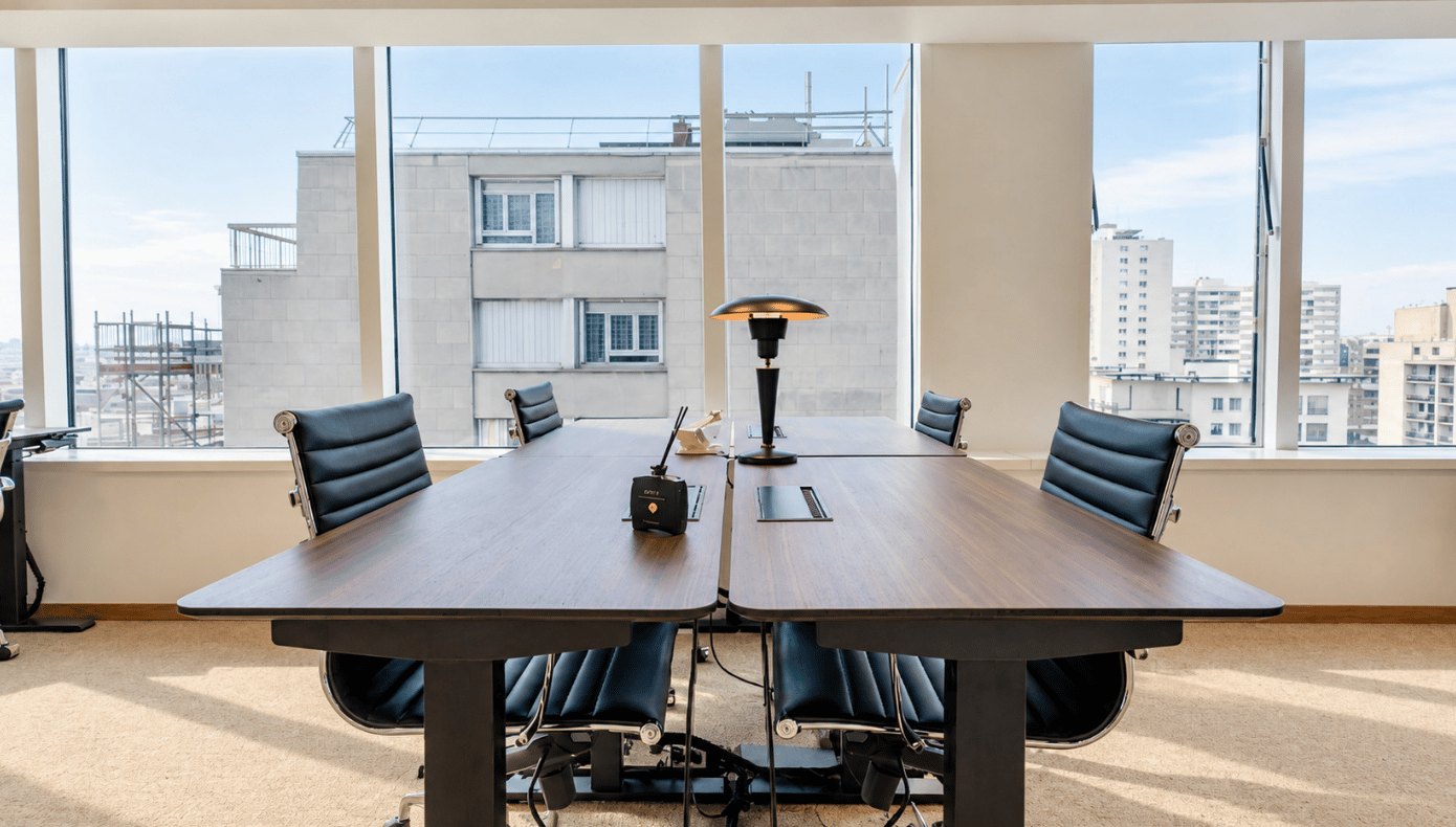 Bureau privatif à Levallois avec grande table en bois, fauteuils noirs et larges baies vitrées.