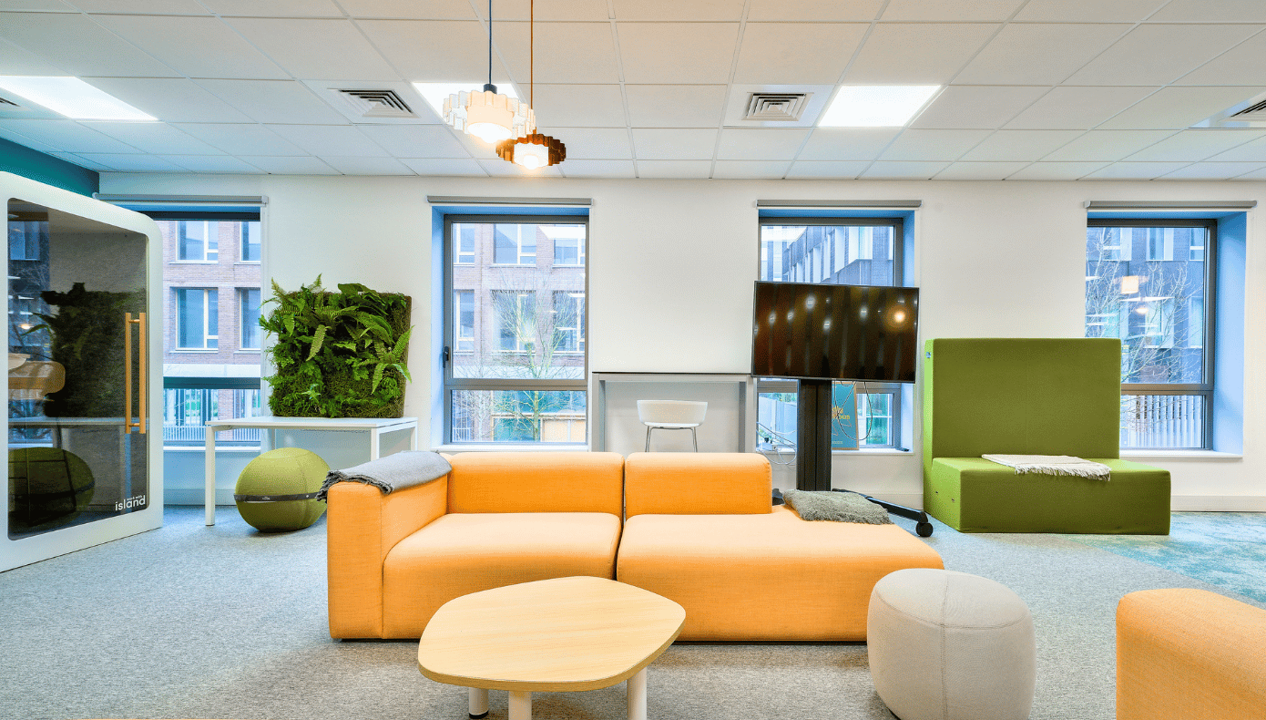 Espace détente Hiptown à Lille avec canapé orange, banquette verte, table basse et mur végétal.
