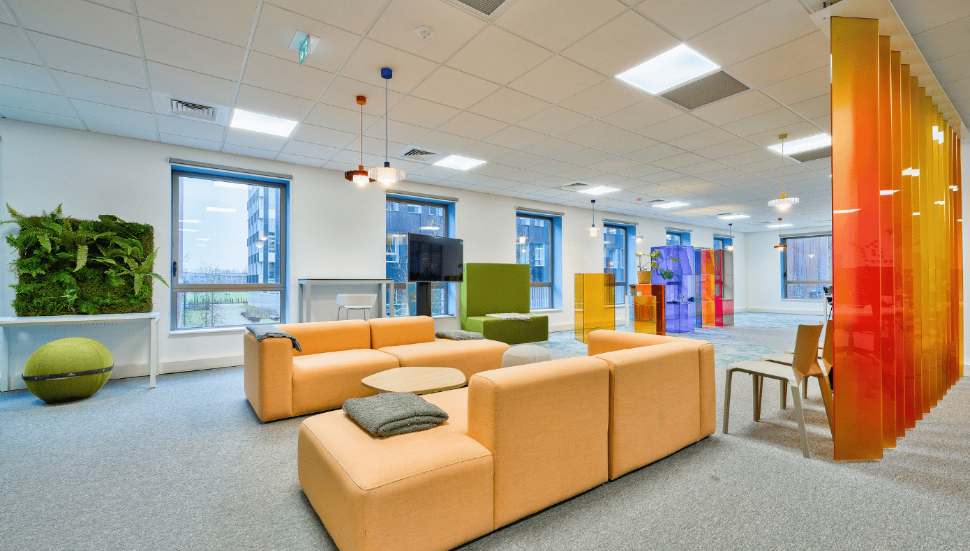Espace détente Hiptown à Lille avec canapés orange, tables basses, cloison colorée et mur végétal.