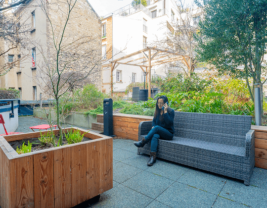 Terrasse extérieure aménagée avec mobilier en rotin et végétation, offrant un espace de détente dans un environnement urbain, au sein des bureaux flexibles Hiptown à Pont Saint-Cloud