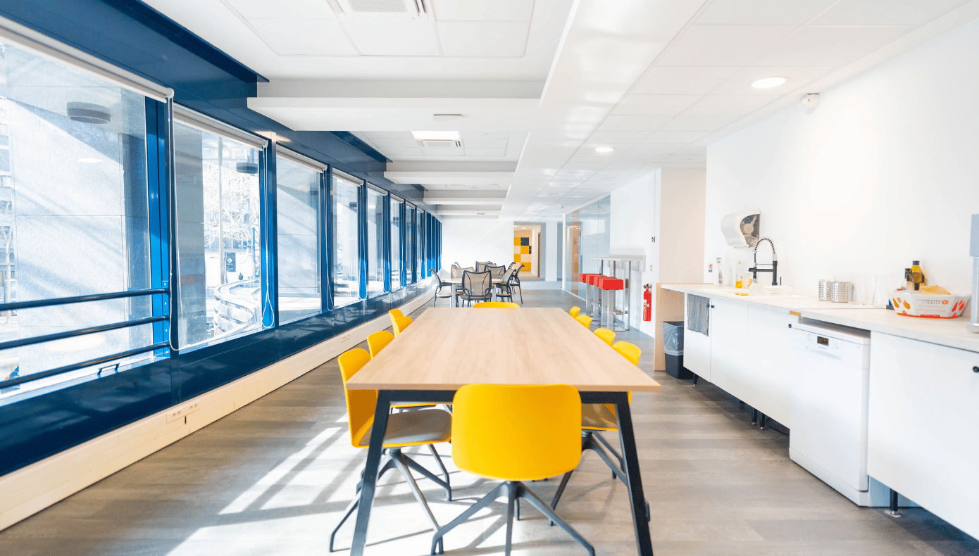 Cafétéria avec table partagée à Boulogne Cafétéria de Hiptown Boulogne avec cuisine équipée, grande table partagée et chaises jaunes près des fenêtres.