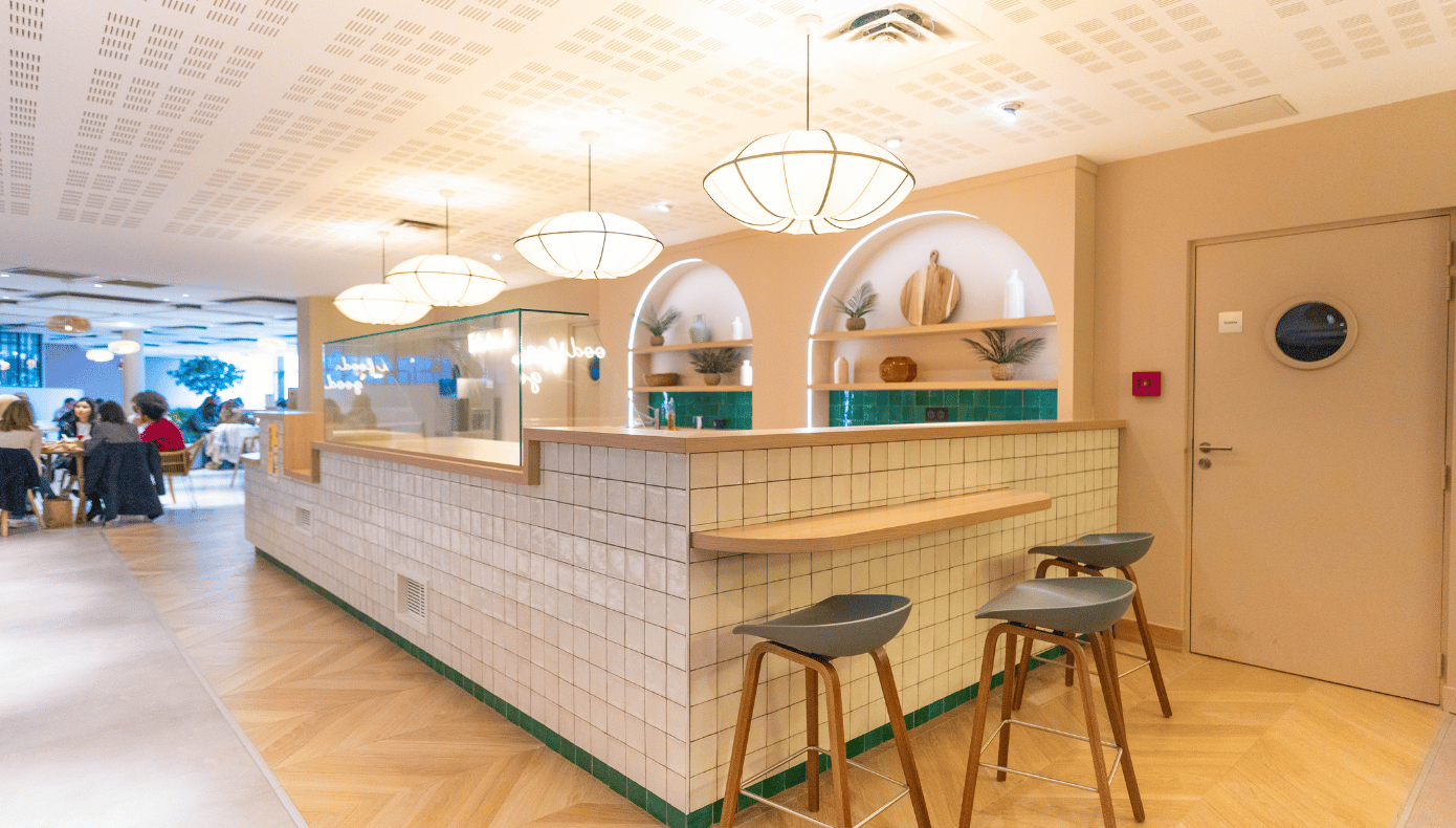 Espace café de Hiptown Boulogne avec comptoir carrelé, tabourets, niches éclairées et suspensions décoratives.