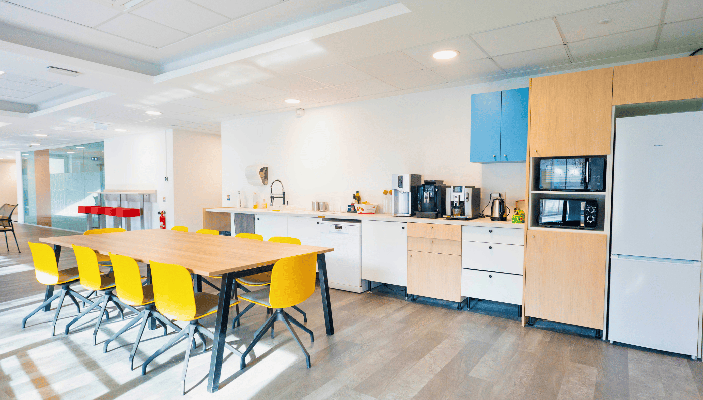 Cuisine équipée de Hiptown Boulogne avec grande table partagée, chaises jaunes et appareils électroménagers.