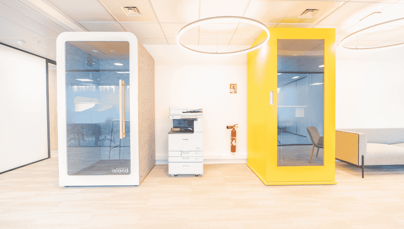 Deux cabines phonebox, dont une jaune, installées près d’un photocopieur et d’un espace détente.
