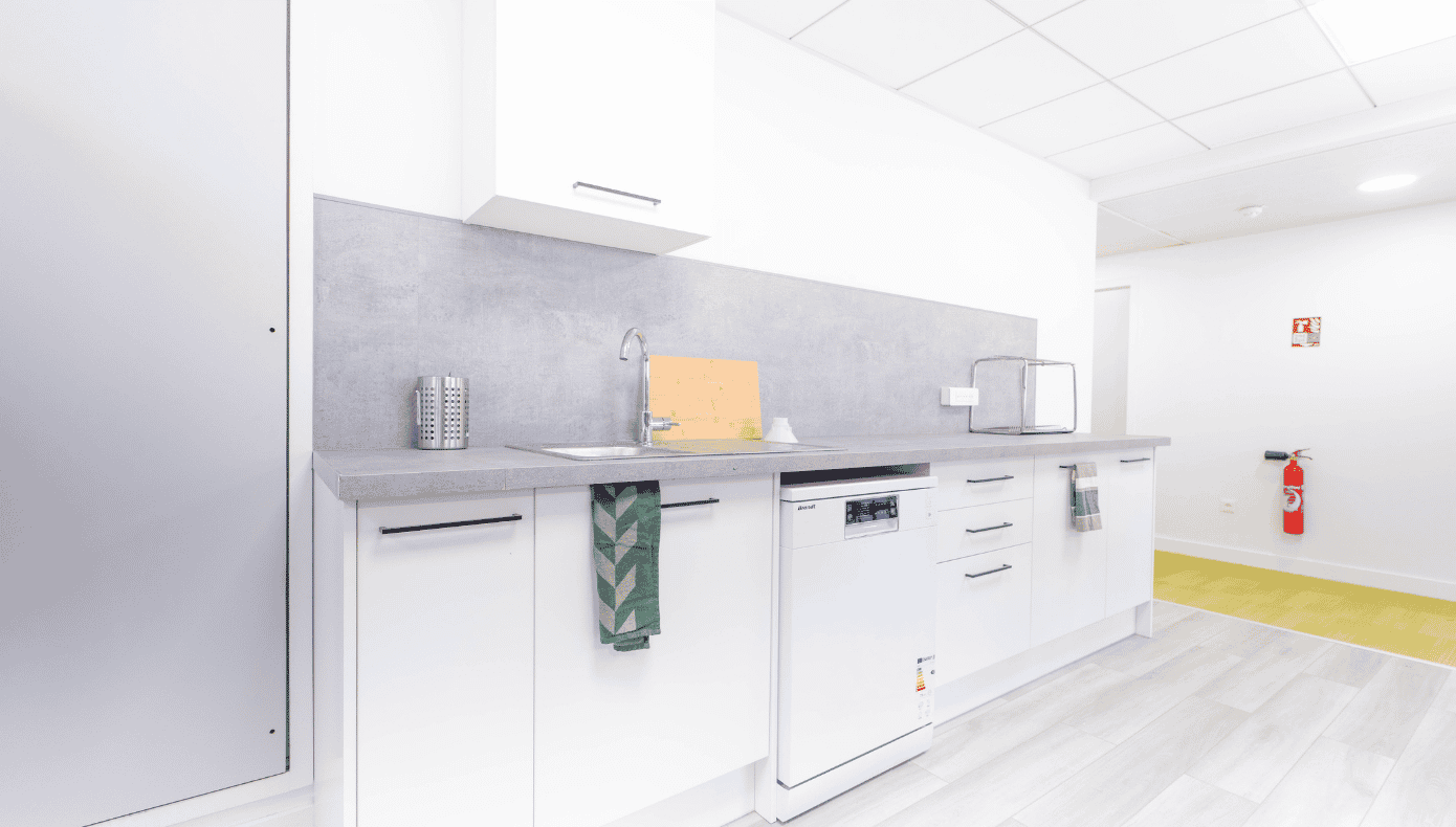 Kitchenette de bureau avec évier, rangements blancs, plan de travail et lave-vaisselle.