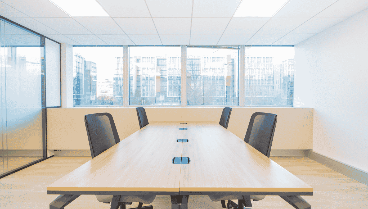 Bureau privatif pour quatre personnes avec longue table en bois et grandes fenêtres sur les bâtiments voisins.