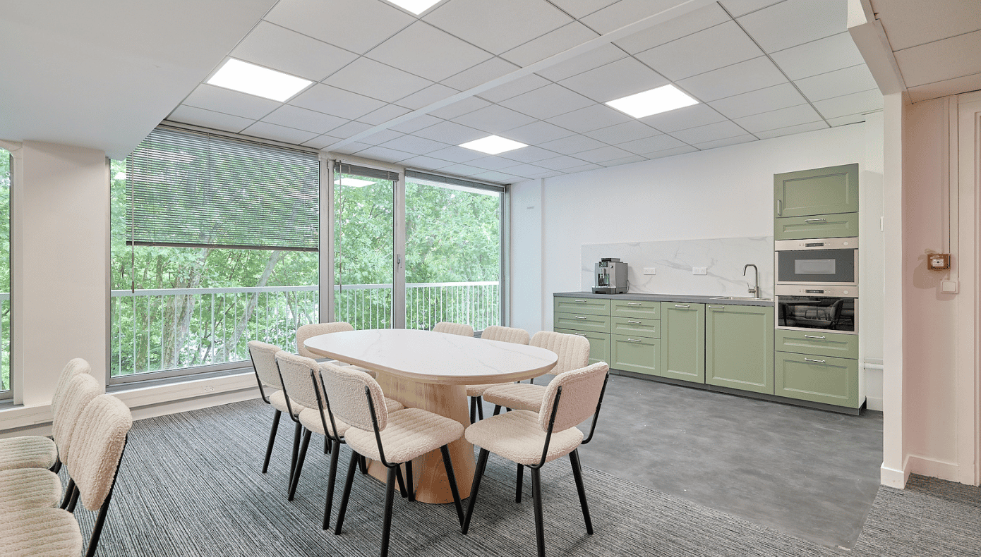 Espace repas de Hiptown Carnot Cuisine partagée avec table, chaises et rangements, bordée de grandes baies vitrées donnant sur les arbres à Saint-Cloud.