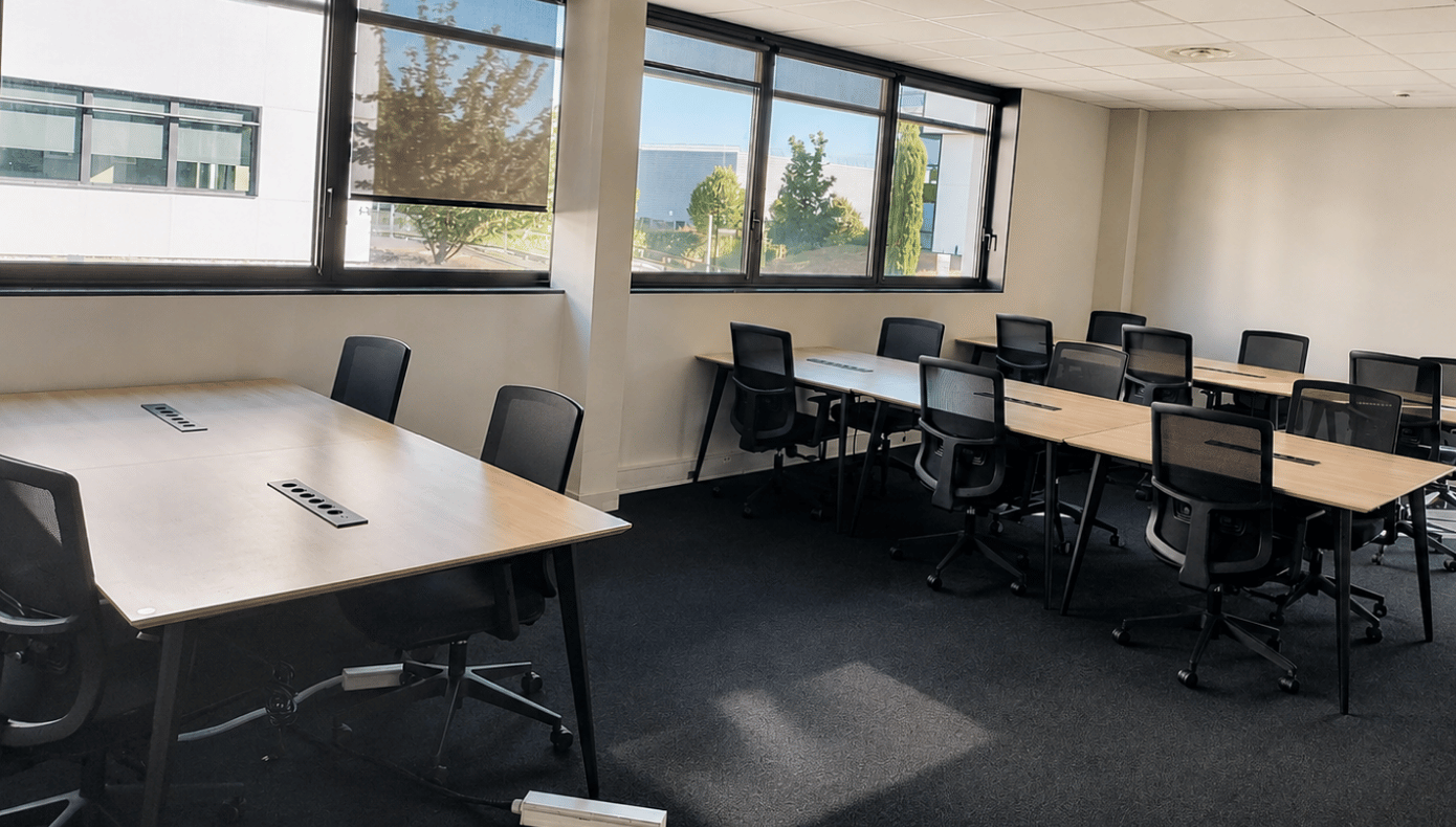 Bureau d’équipe avec deux groupes de tables, plusieurs sièges mobiles et une fenêtre donnant sur la végétation.