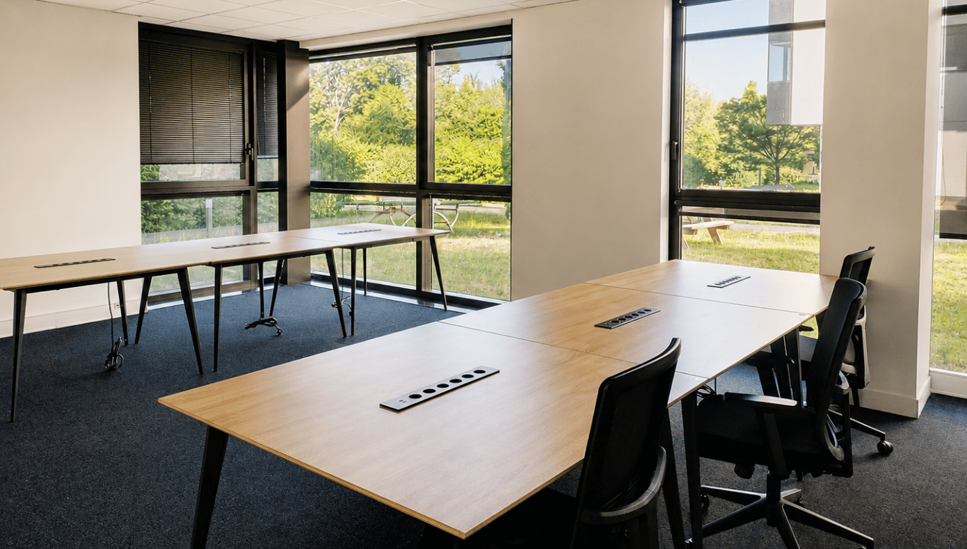 Espace de travail avec grandes tables équipées, baies vitrées et vue directe sur les espaces verts extérieurs.
