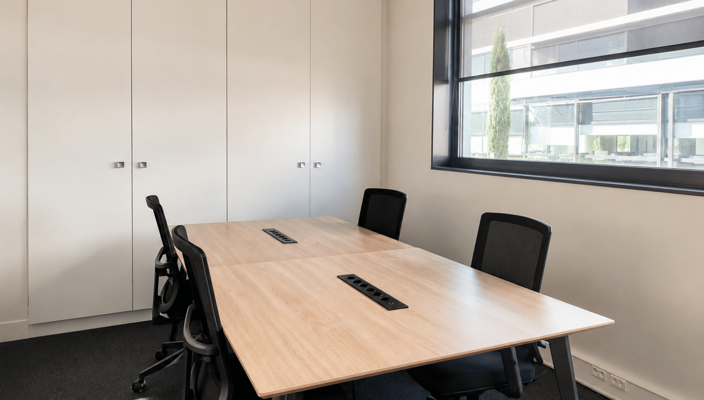 Petit espace de travail avec table centrale, quatre sièges, rangements intégrés et fenêtre donnant sur le site.