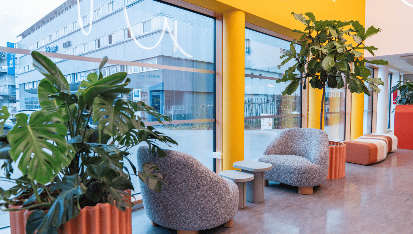 Hall d’accueil à Pantin avec fauteuils, petites tables, plantes et grandes baies vitrées.