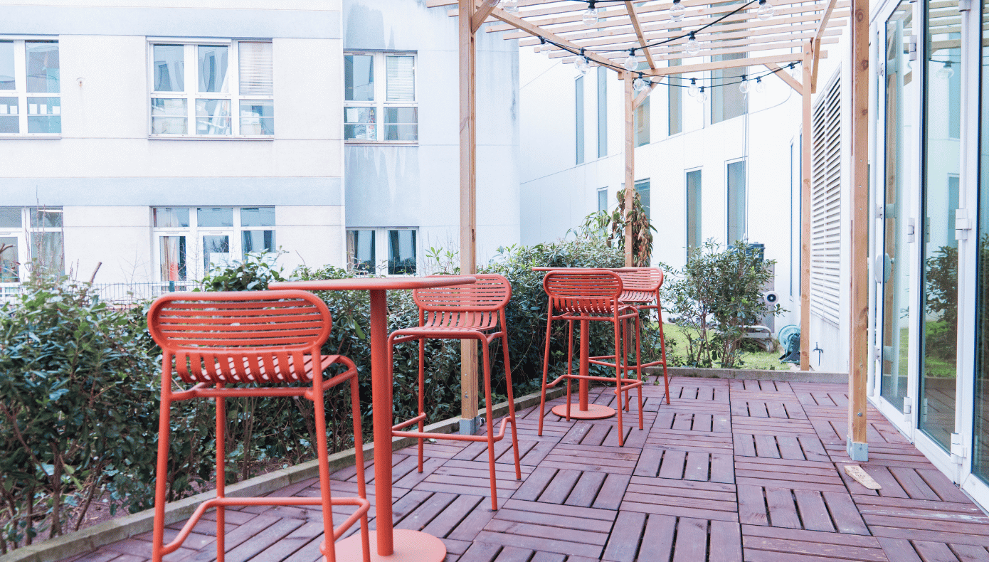 Terrasse extérieure à Pantin avec tables hautes, chaises rouges, pergola en bois et végétation.